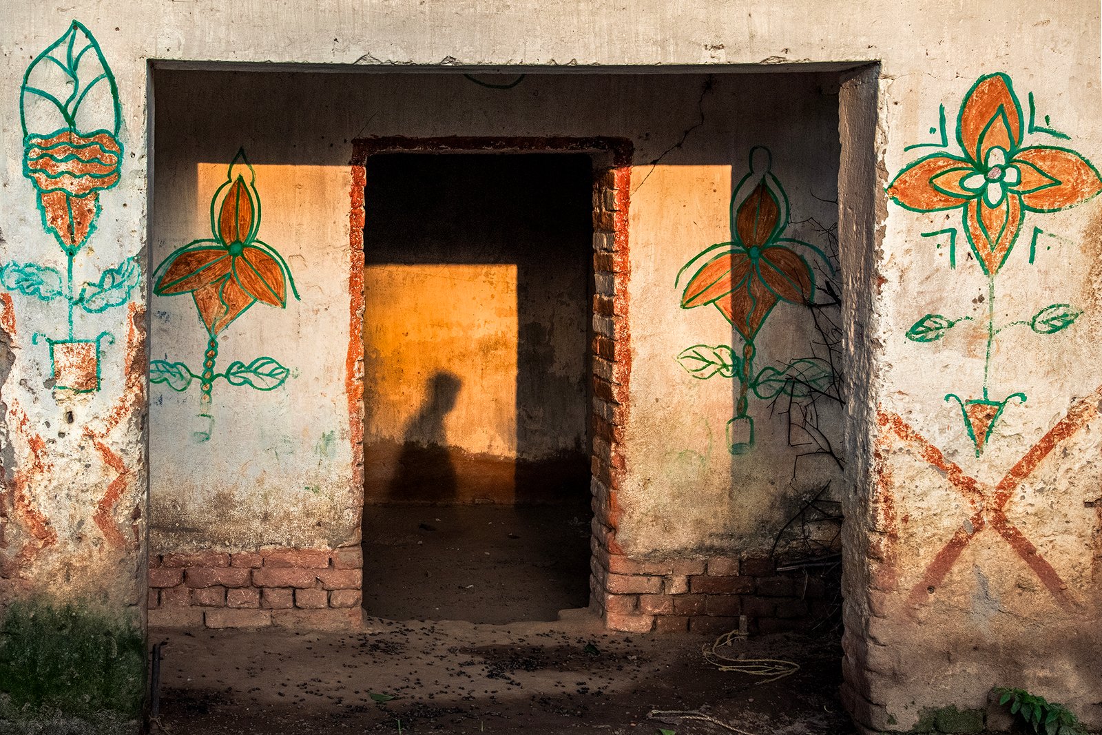 Arpan Dutta Chowdhury: Black, White & In Between 3 Warm light casts a child’s shadow inside a doorway framed by hand-painted floral motifs on a weathered wall.