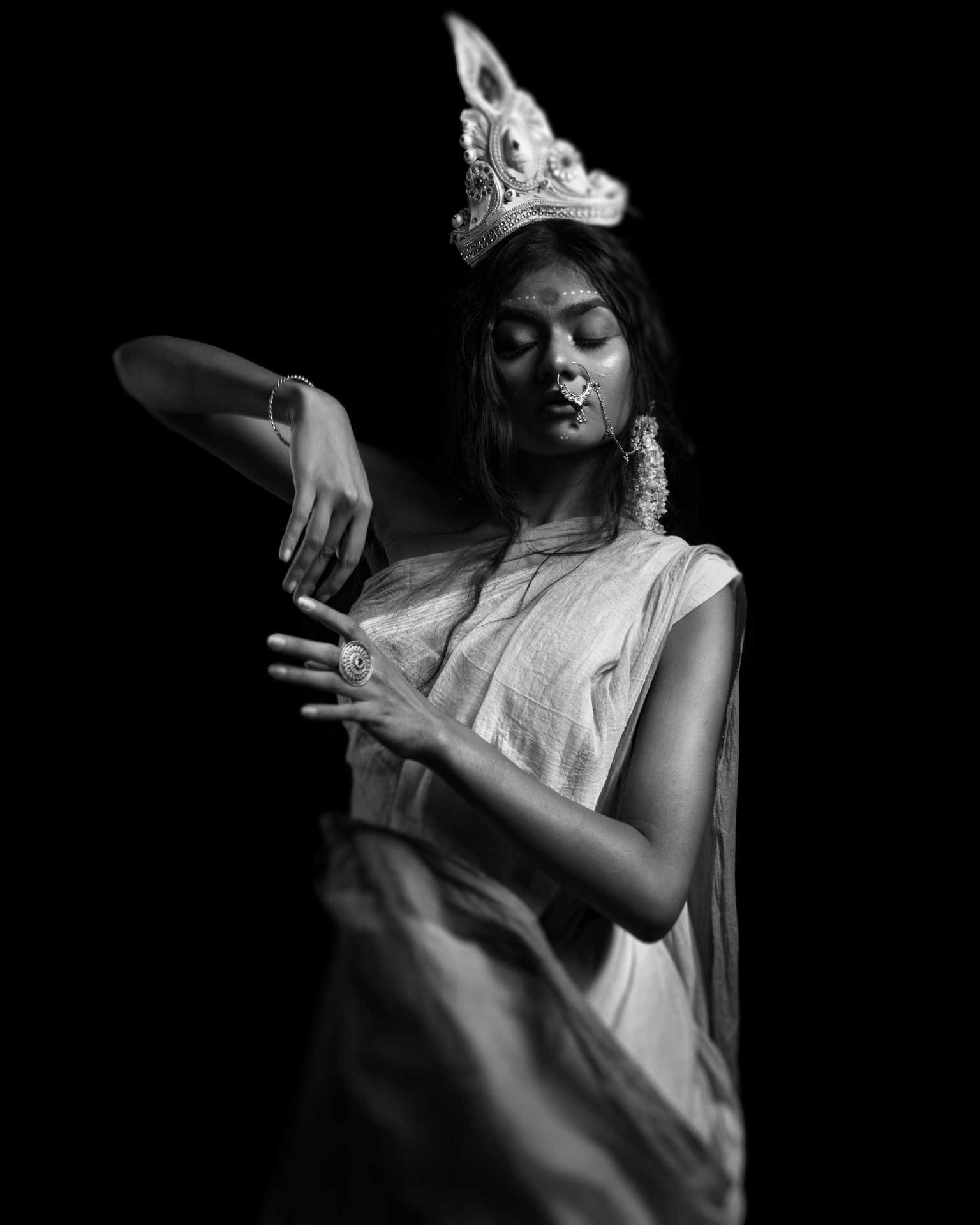 Arpan Dutta Chowdhury: Black, White & In Between 6 Woman in crown and sari performs a graceful mudra against a black background; scarf blurred, black-and-white.