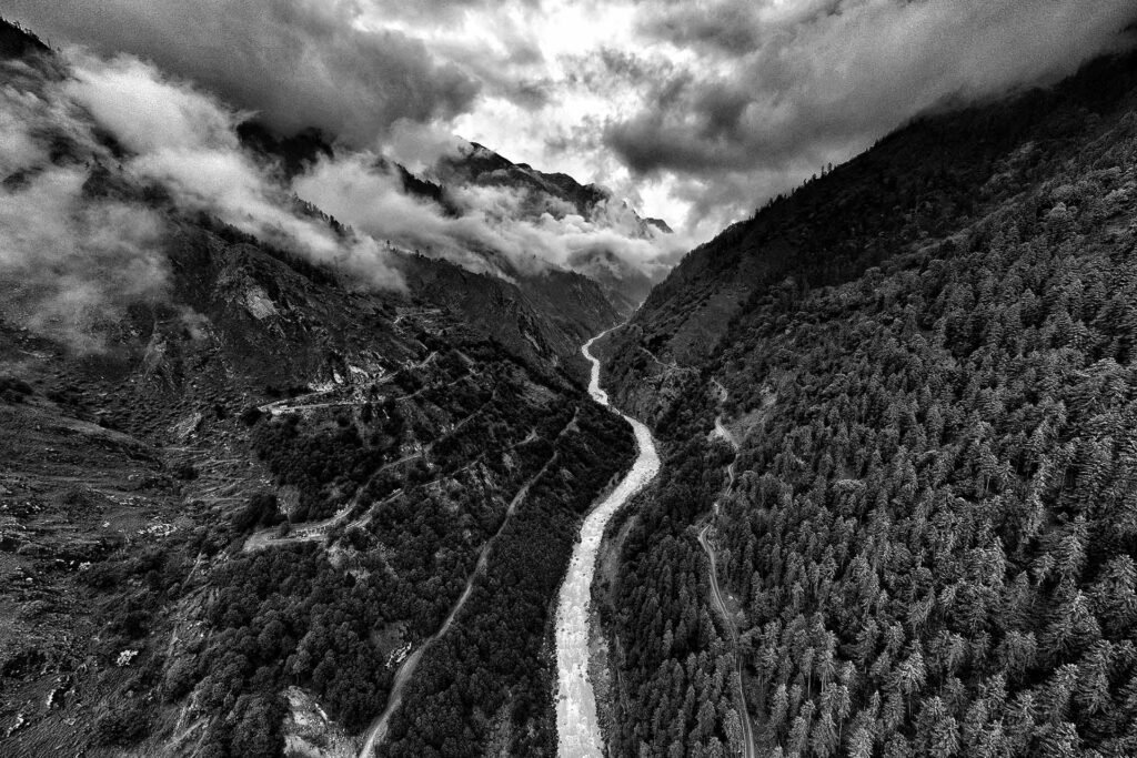 Arpan Dutta Chowdhury: Black, White & In Between 1 Aerial view of a river carving through steep forested valleys under heavy clouds, black-and-white.