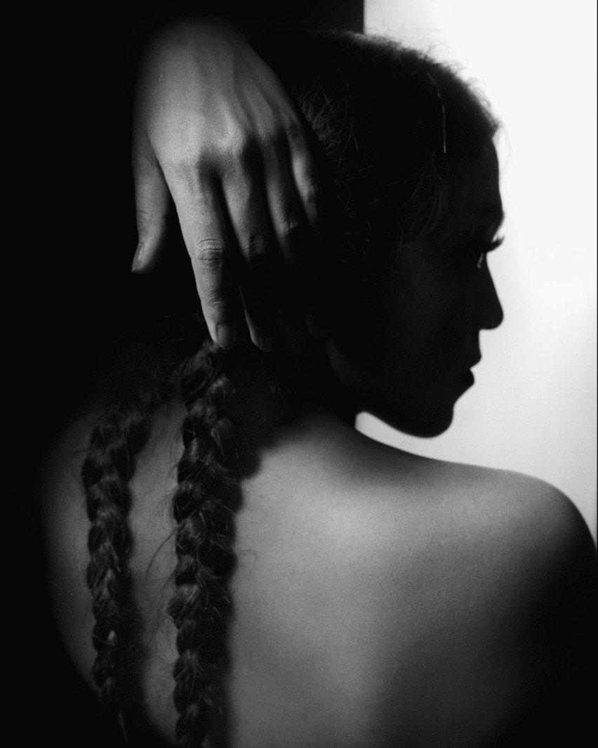 Arpan Dutta Chowdhury: Black, White & In Between 7 Backlit silhouette of a woman’s back with two braids as her hand touches her head, high-contrast black-and-white.